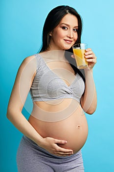 Pregnant caucasian model with long black hair holding a glass of fresh juice.