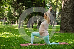 Pregnant caucasian woman doing yoga in the park. Warrior Pose.