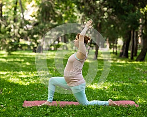 Pregnant caucasian woman doing yoga in the park. Warrior Pose.