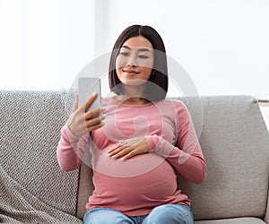 Pregnant Chinese Lady Using Phone Making Selfie Sitting At Home