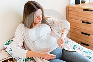 Pregnant contractions time. Pregnancy woman watching clock, holding baby belly. Childbirth time, contractions pain