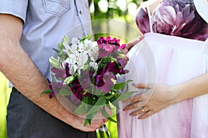 Pregnant couple with bouquet of flowers in a summer park