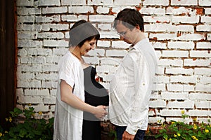 Pregnant couple comparing the size of their big belly, maternity concept portrait, on grey background