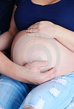 A pregnant couple embraces a woman with a stomach, close-up. Close-up of a human couple holding a pregnant belly in