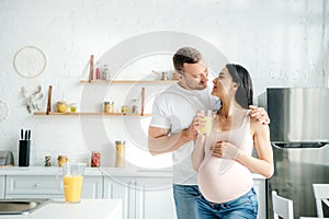Pregnant couple holding orange juice in kitchen