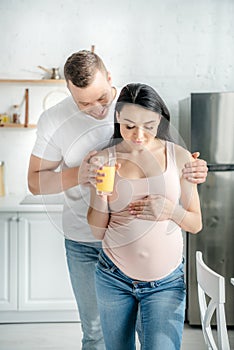 Pregnant couple hugging and holding orange juice in kitchen