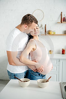 Pregnant couple hugging in kitchen with cereals in bowls