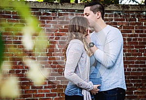 Pregnant couple kissing in front of brick wall