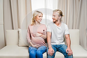 Pregnant couple sitting together on sofa and smiling each other