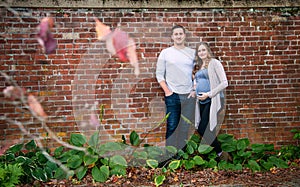 Pregnant couple standing in front of brick wall