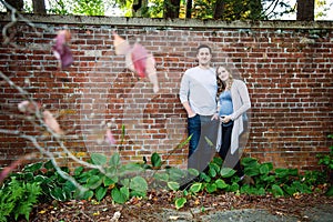 Pregnant couple standing in front of brick wall
