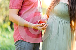 A pregnant couple standing outdoor holding an apple in their hands. Close up, soft selective focus.