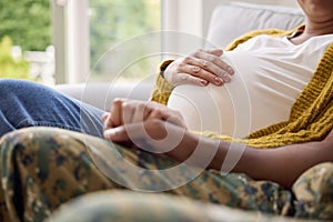 Pregnant Couple With Woman Sitting Next To Army Husband In Uniform Holding Hands Home On Leave 