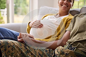 Pregnant Couple With Woman Sitting Next To Army Husband In Uniform Holding Hands Home On Leave 
