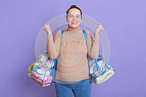 Pregnant European woman with hair bun leaving for maternity hospital, expressing joy and happiness, clenched fists, wearing beige