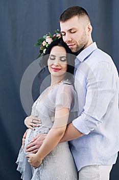 Pregnant european woman with her husband on gray background, young european couple waiting for a child, prenant woman