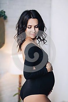 Pregnant european woman in white apartment, young european woman waiting for a child, prenant woman with black hair in
