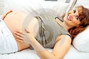 Pregnant female lying on sofa and holding belly
