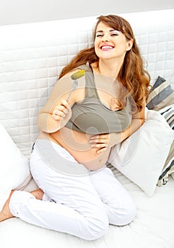 Pregnant female sitting on divan and eating pickle