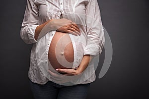 Pregnant girl with a bare belly on gray background.