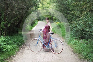 Pregnant girl with bicycle on a forest road, soft focus, side vi