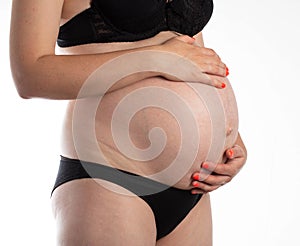 Pregnant girl in black underwear on a white background. Third trimester of pregnancy. Preparation for childbirth, hormones