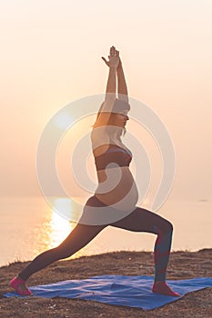 Pregnant girl is doing yoga on the beach