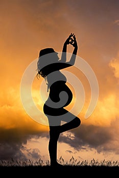 A pregnant girl doing yoga at sunset