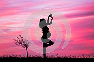 A pregnant girl doing yoga at sunset