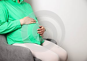 A pregnant girl in a green blouse sits on a chair and counts regular contractions before the onset of labor and a trip