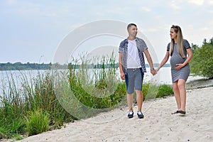 A pregnant girl and a guy walking along the river bank