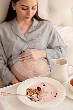 A pregnant girl is having breakfast in bed