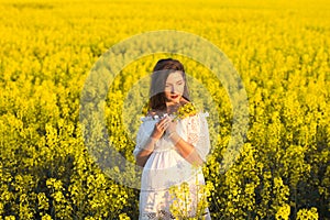 Pregnant girl holding flowers. Belly of a pregnant woman. The concept of pregnancy. Over green nature blurred background. Pregnant