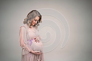 A pregnant girl is holding her belly. A young mother is expecting the birth of a child. Woman gently hugs her baby in