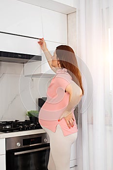 A pregnant girl in the kitchen who has pain and discomfort in her stomach and lower back. Malaise during pregnancy