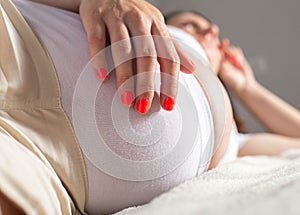 a pregnant girl lies on the bed and holds her stomach. Abdominal discomfort and pain concept. Exacerbation of chronic photo