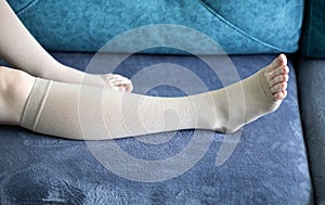 A pregnant girl lies at home on a blue sofa in compression stockings for varicose veins. Pain and swelling in the legs