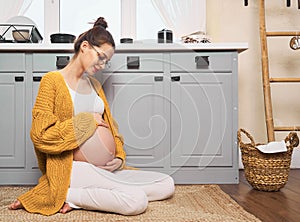 A pregnant girl with a naked belly sits on the kitchen floor