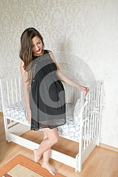 Pregnant girl near the bed for a child. kravatka white color for the child. preparing for the birth of a child. photo of a