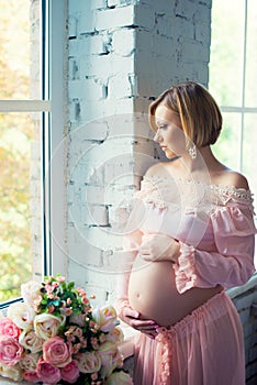 Pregnant girl near the window hugging tummy. Happy 9 months of pregnancy and waiting baby