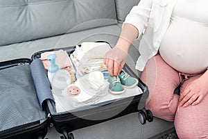 A pregnant girl packs her things and cute little shoes into a suitcase