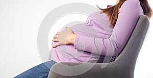 A pregnant girl sits in a chair and holds on to her stomach. The concept of fatigue and malaise during pregnancy. Uncomfortable