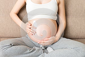 A pregnant girl sits at home on the bed and smears an anti-stretch mark cream on her stomach. Pregnancy, motherhood, preparation