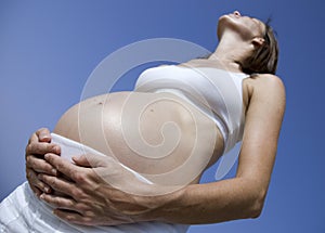 Pregnant girl standing up against a blue sky