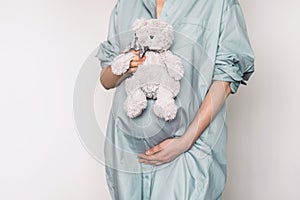 Pregnant girl touching belly and teddy bear toy resting, awaiting the child birth. Woman expecting baby. Natural
