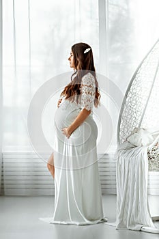 A pregnant girl in white clothes stands on a light background. Beautiful belly of a young attractive pregnant girl. Family,