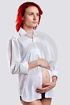 Pregnant girl in a white shirt hugging her tummy. White background.