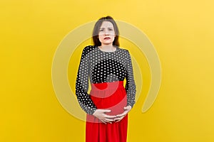a pregnant girl who has a stomach ache stands on a colored background. 