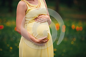 Pregnant girl in a yellow dress hugging her stomach in the field