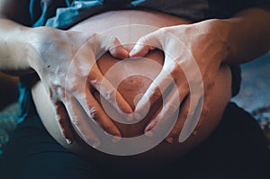 Pregnant hands making a heart on her belly
